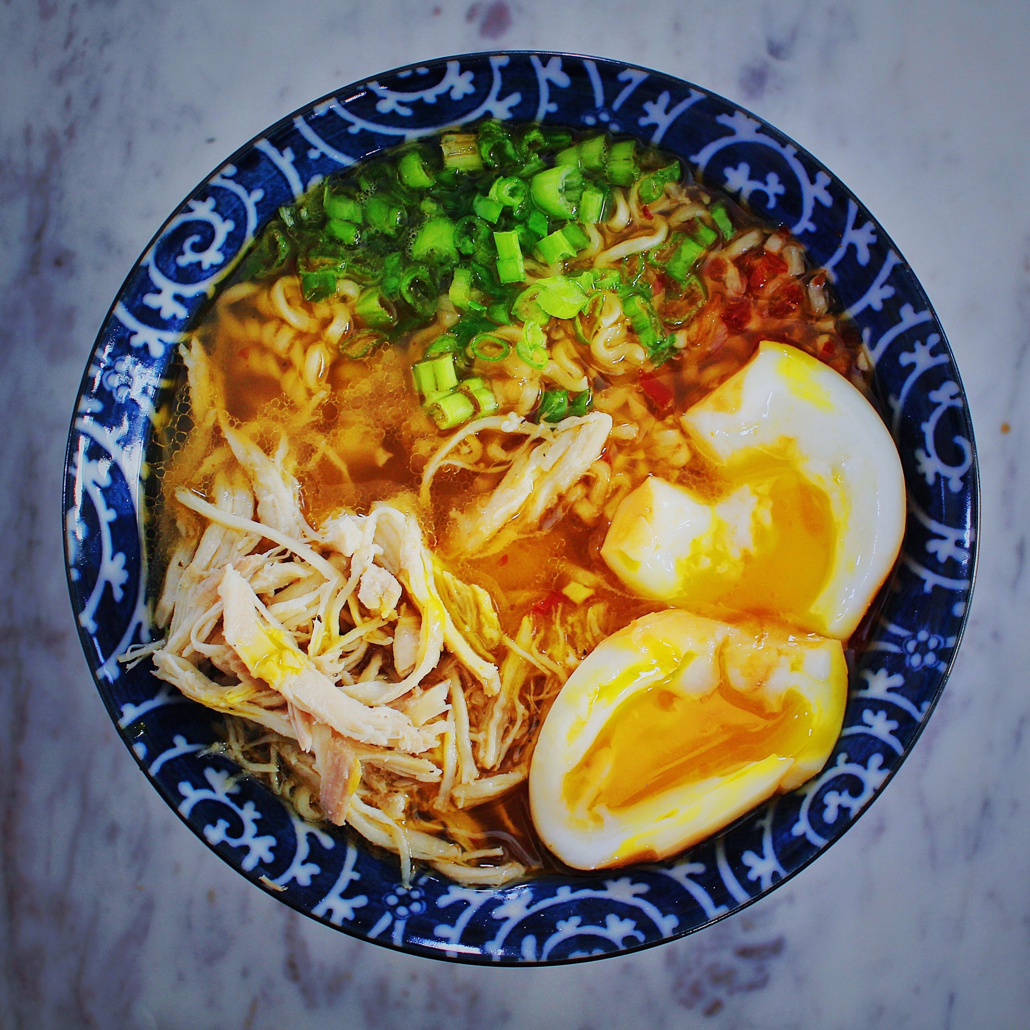 a bowl of ramen with shredded chicken, a soft-boiled egg, and scallions
