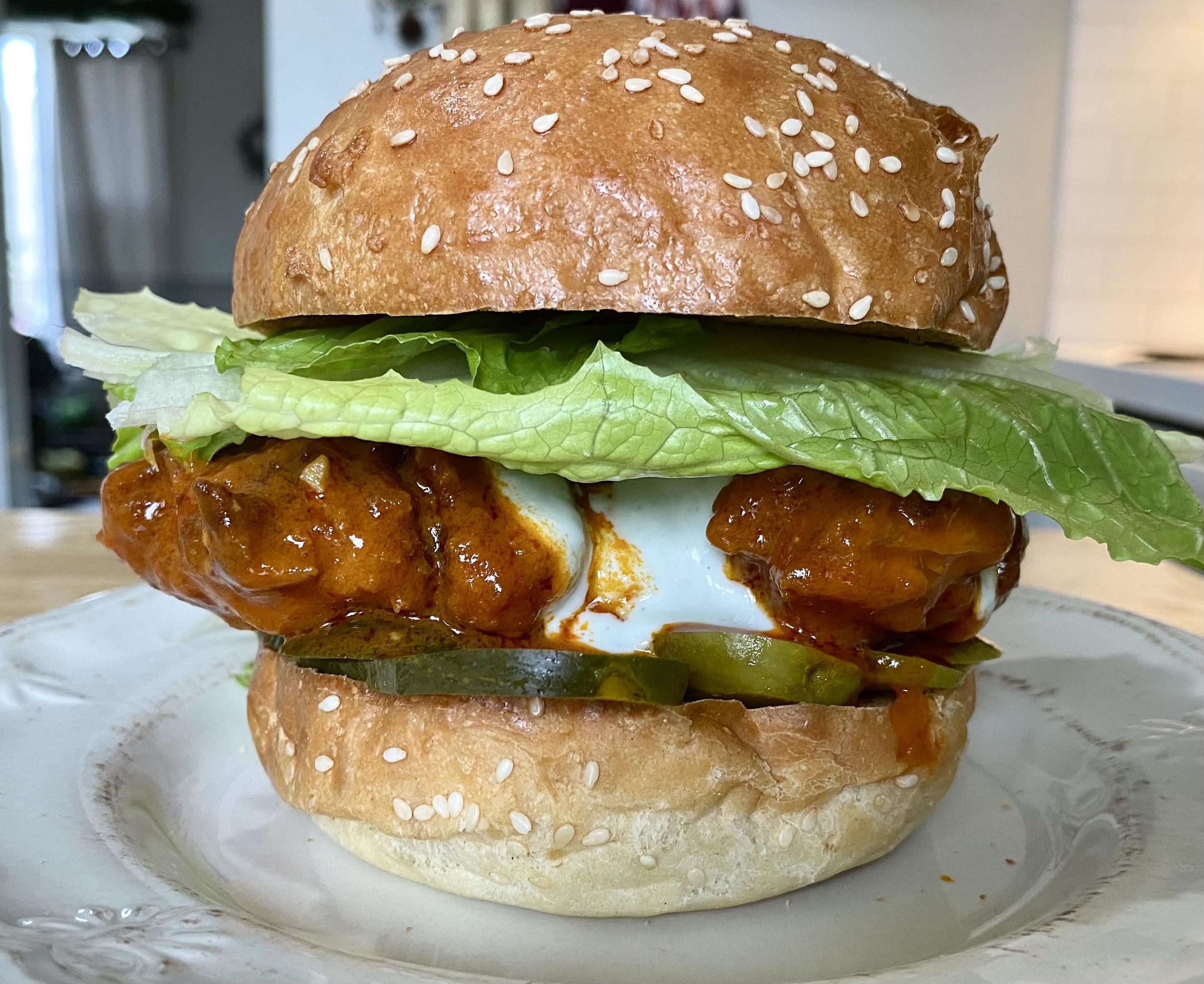 a buffalo chicken sandwich with a large lettuce leaf, pickles, and blue cheese dressing