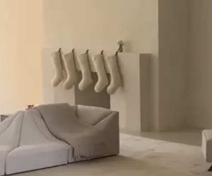Beige stockings hanging from a beige fireplace near a beige seating area with a beige throw on it and with a beige rug