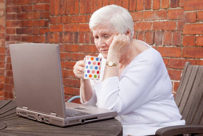Older woman holding a mug and looking at a laptop screen