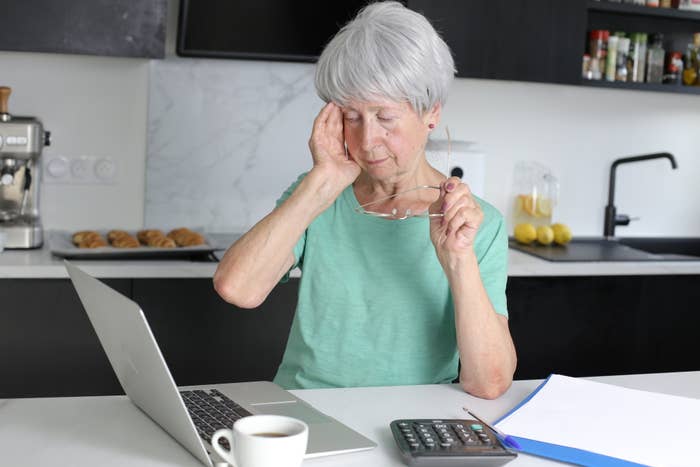 An older woman looking at her laptop and touching her face