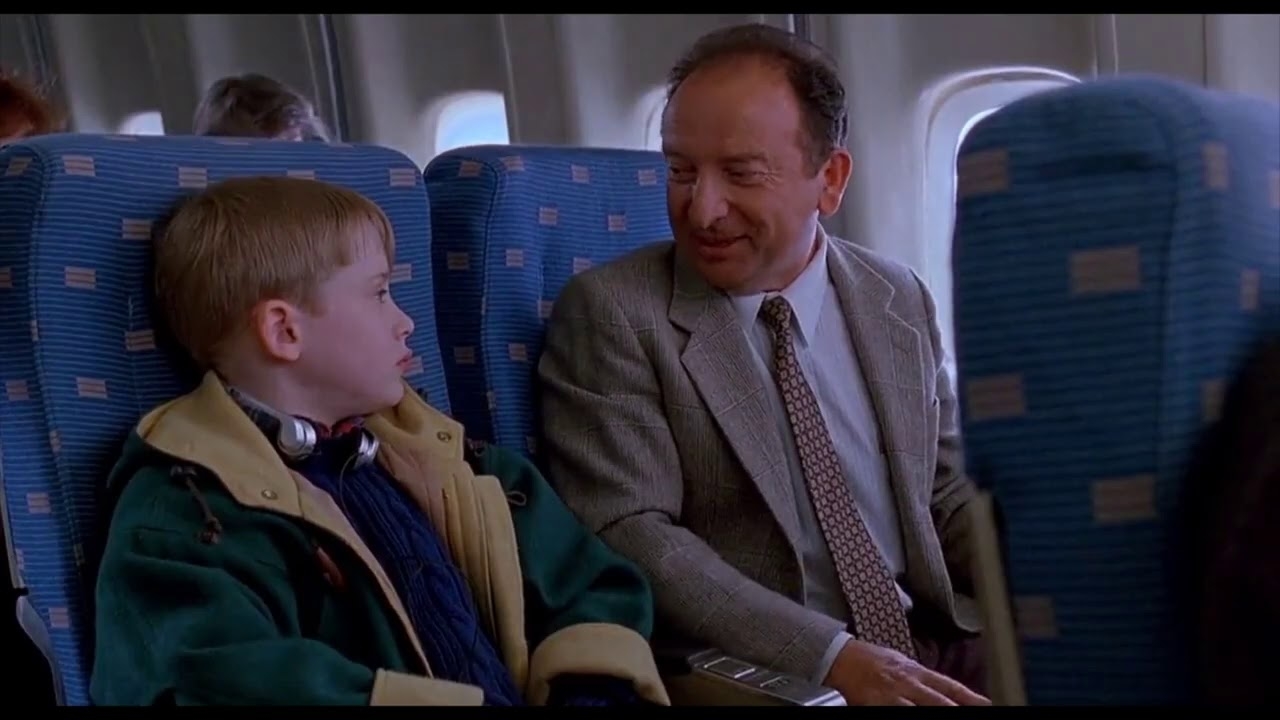 Kevin McAllister from Home Alone 2 in an airplane seat talking to a man in a suit and tie