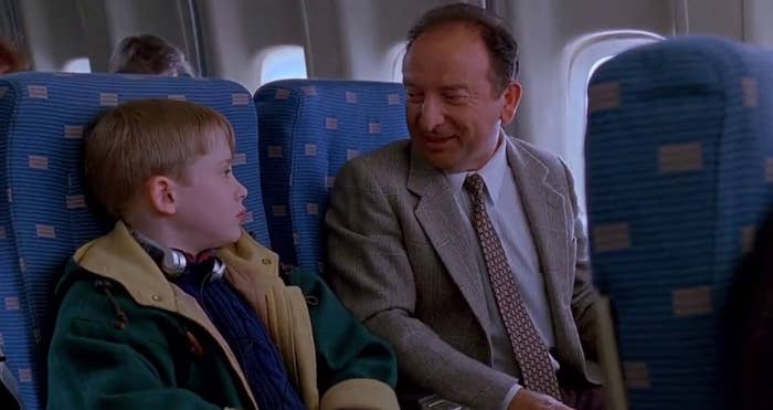 Kevin McAllister from Home Alone 2 in an airplane seat talking to a man in a suit and tie