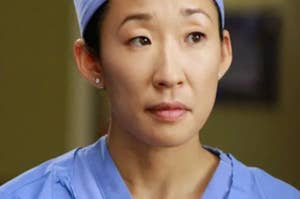 A screencap of Sandra Oh depicting Cristina Yang in the tv show "Grey's Anatomy" wearing doctor's gown and cap