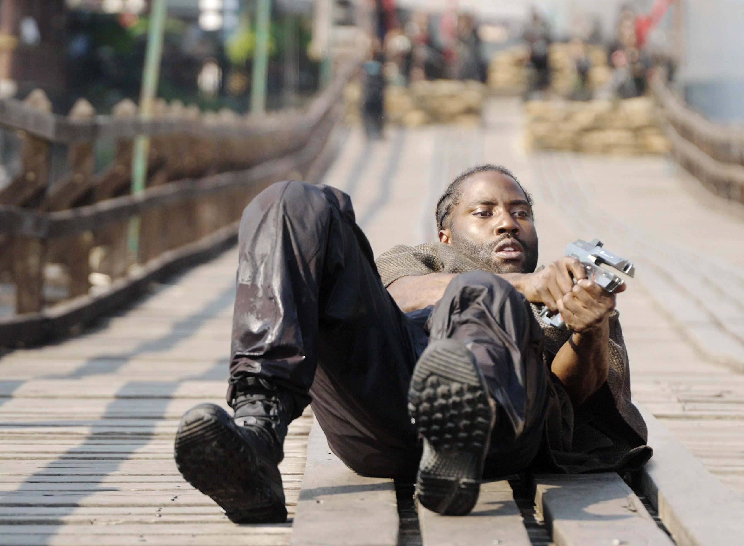 A man lying on a bridge and holding a gun