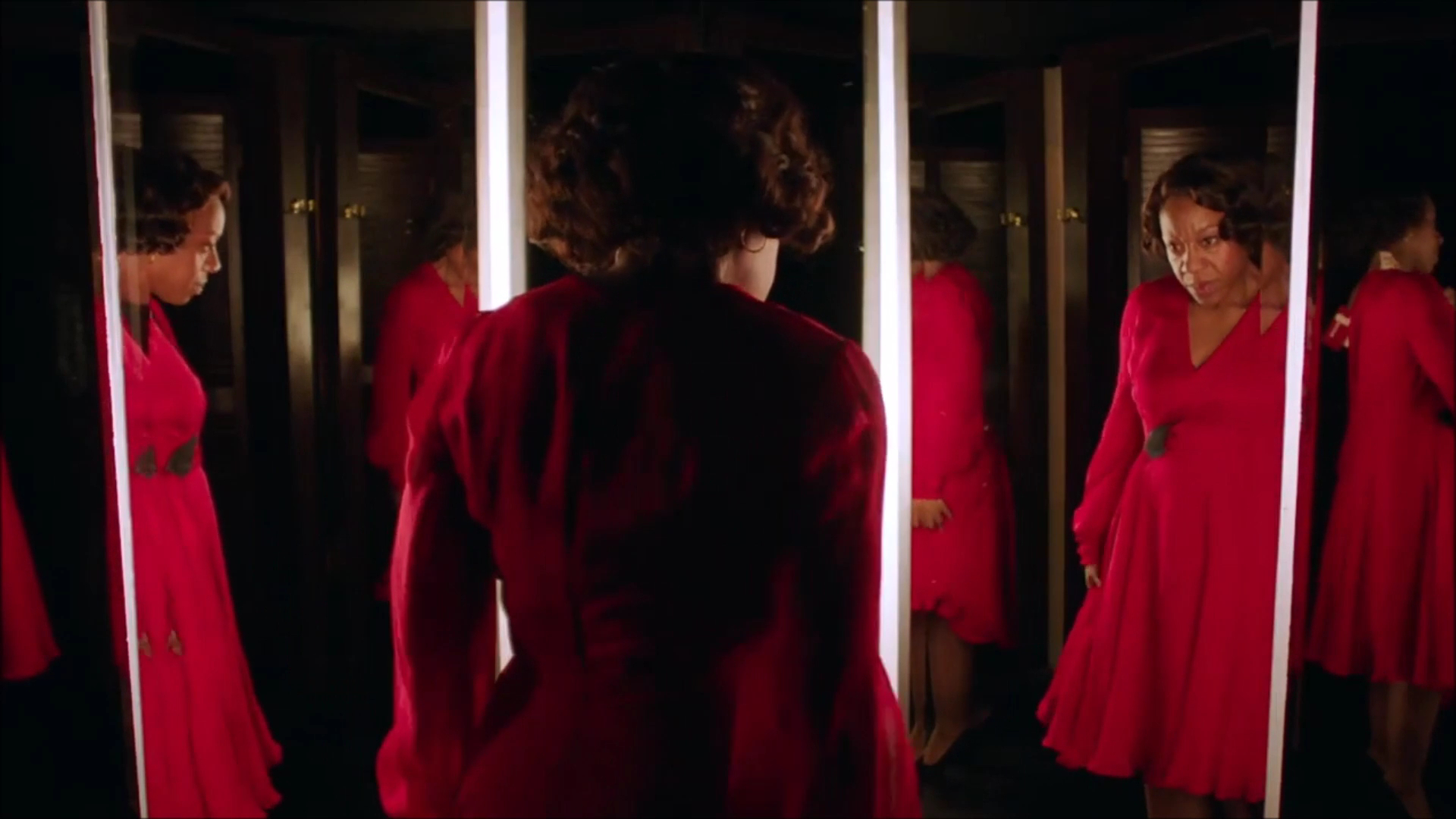 Marianne Jean-Baptiste trying on a red dress in front of multiple mirrors.