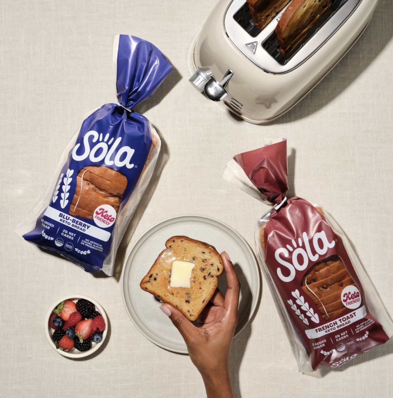 Model holding bread surrounded by two bread bags, a bowl of fruit, and a toaster.