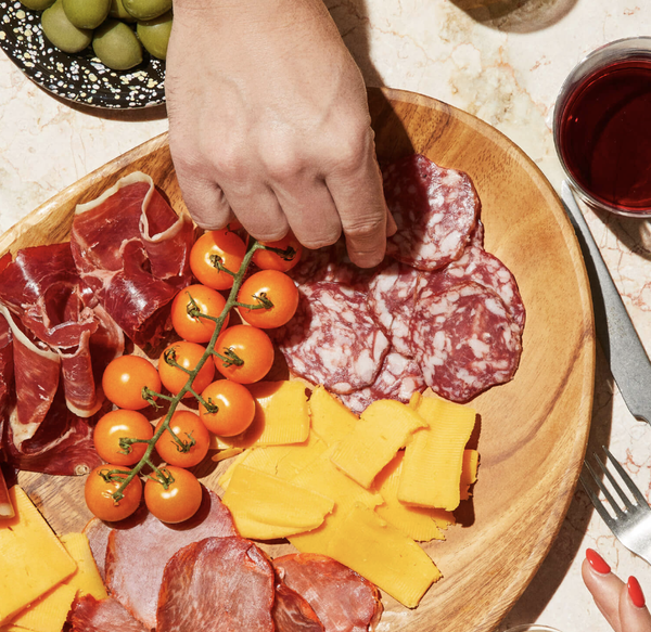 Hand taking food from a charcuterie board.