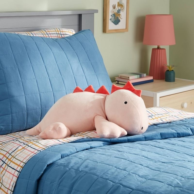 a pink dinosaur weighted pillow on a bed
