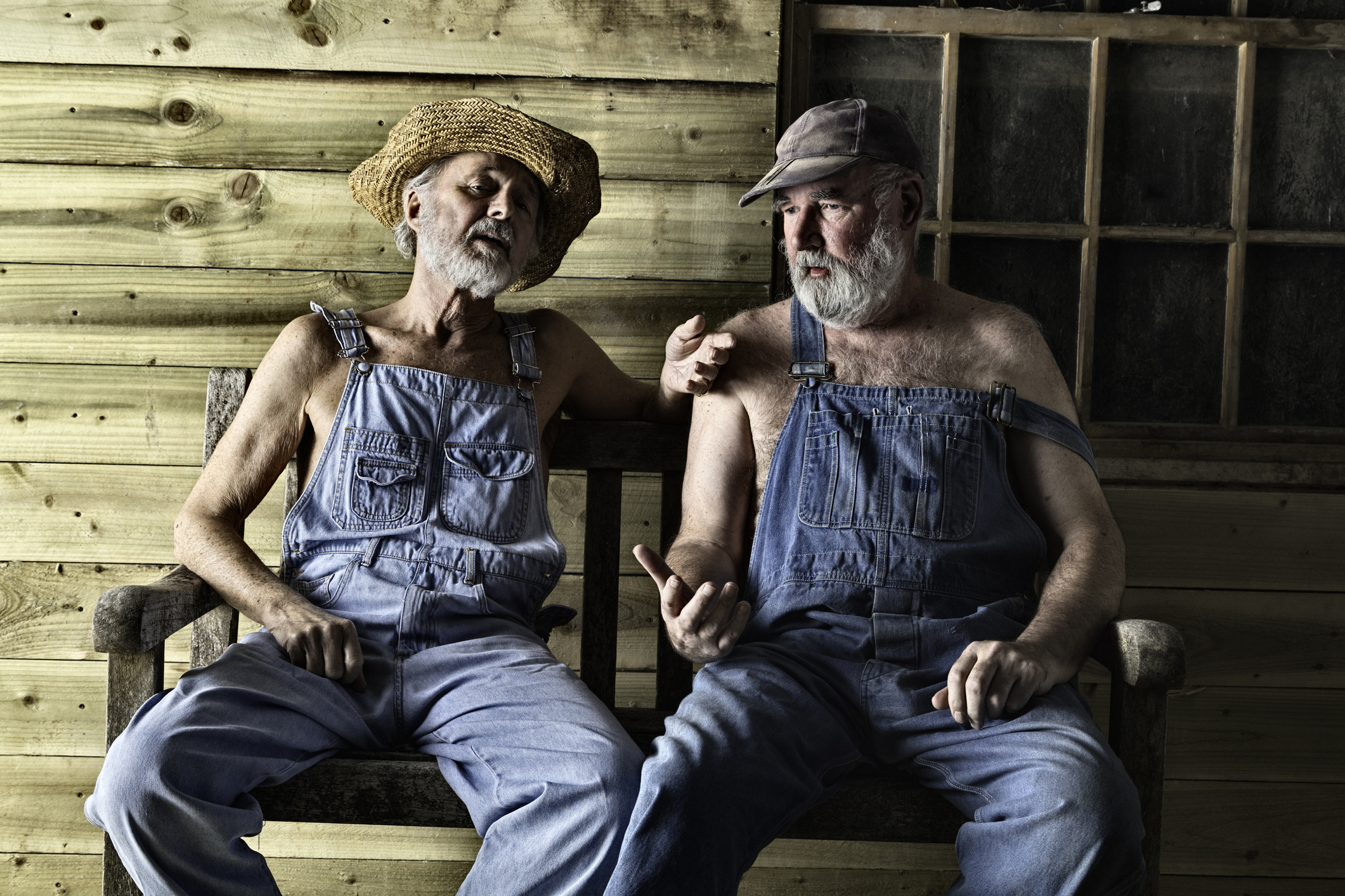 two older men sitting down wearing overalls