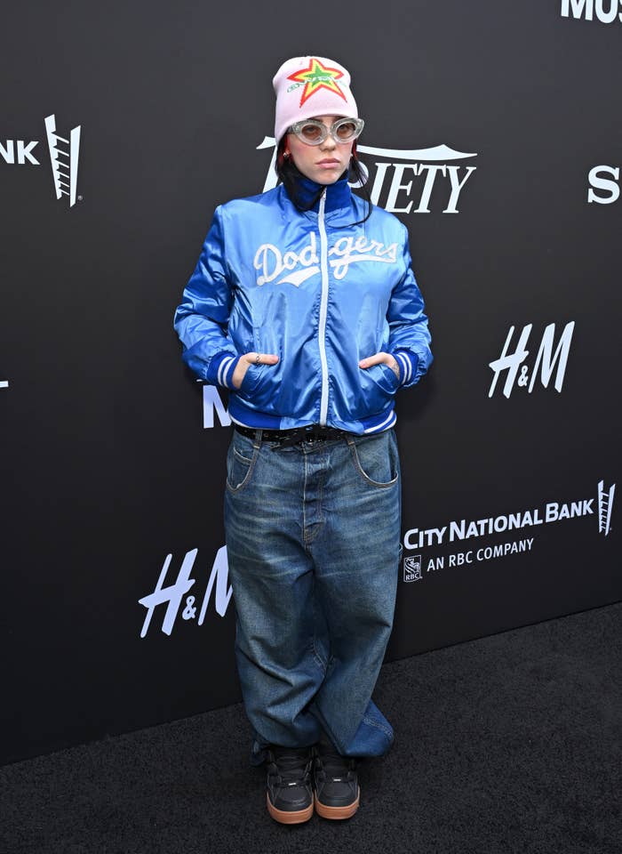 Closeup of Billie Eilish at a media event in a Dodgers jacket and jeans