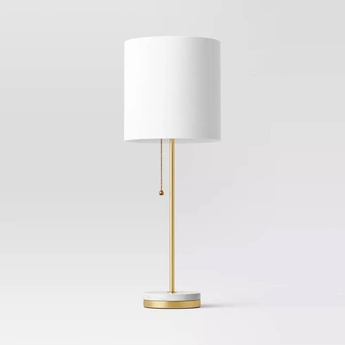 Floor lamp with a white shade and a gold base with a pull chain, against a plain background