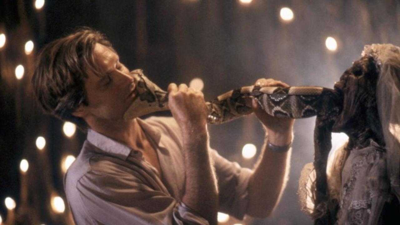 Bill Pullman kissing a snake as it emerges from the mouth of a skeleton in a white dress.