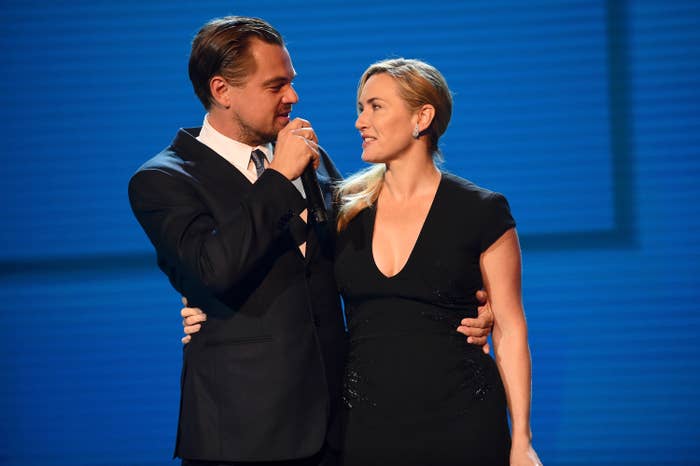 Le and Kate onstage with their arms around each other as Leo speaks into a microphone