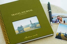an olive green travel journal and photos laid out on a table