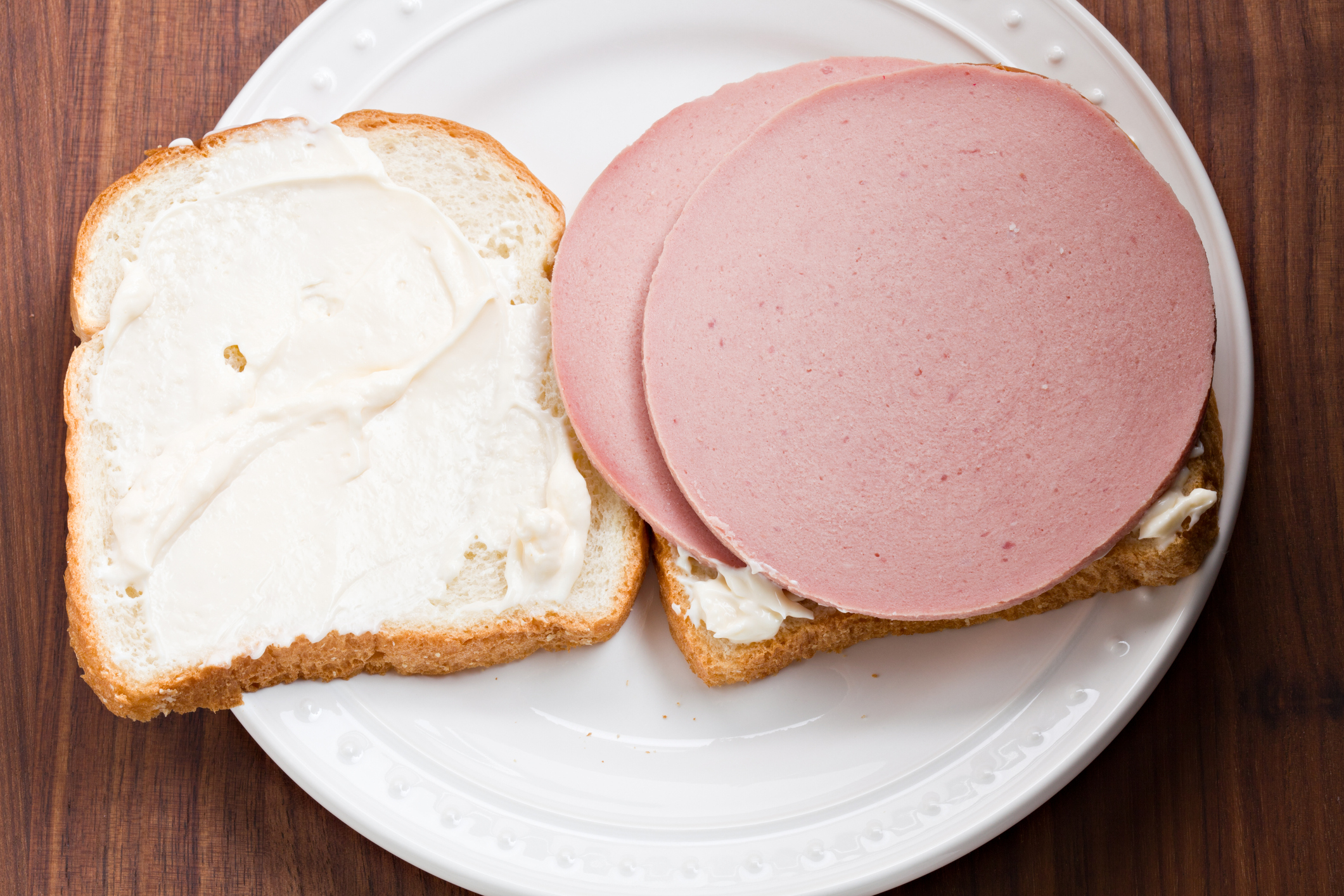 An overhead close up view of a dinner plate with an open face bologna sandwich on white sourdough bread
