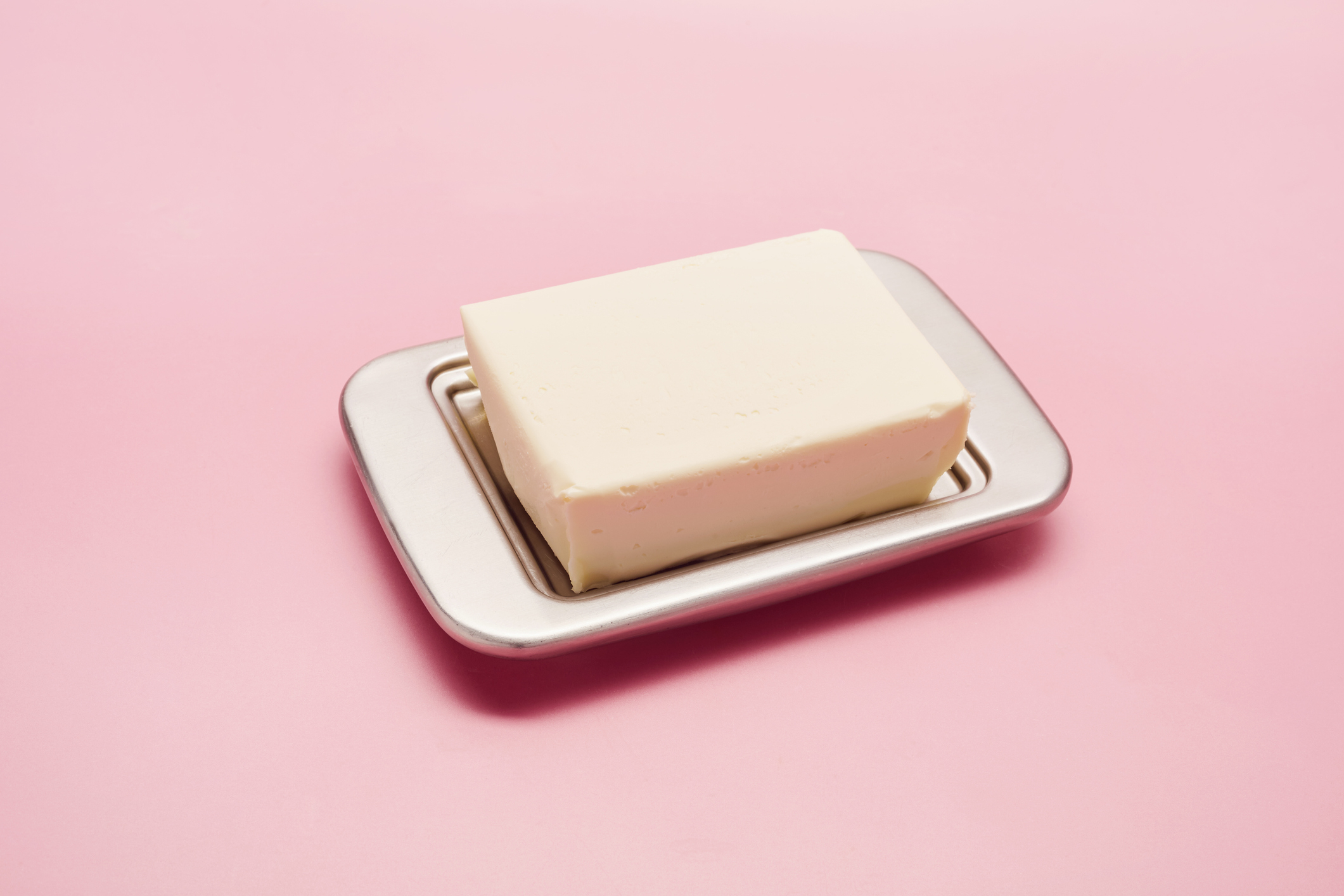 A slab of butter on a silver platter, photographed over a colored background