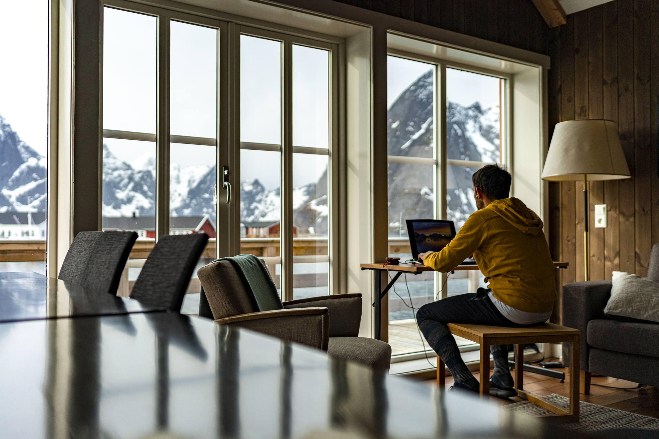 A young person working on a laptop in front of a big window with a mountain view