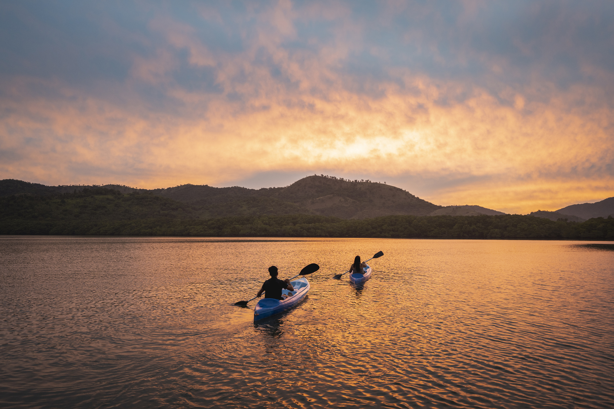 Two kayakers paddling in a large body of water at sunset