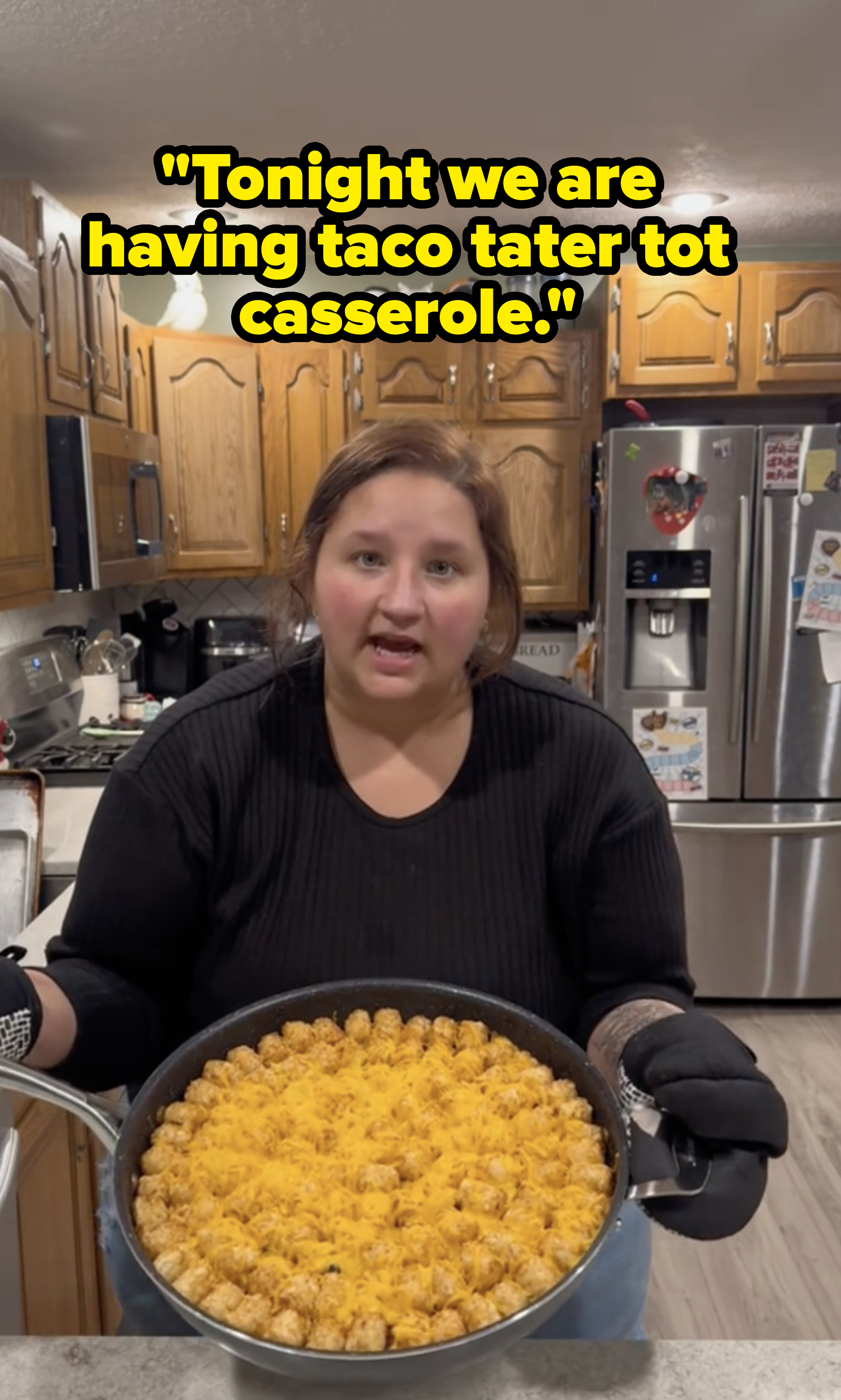 a tiktok creator standing holding up a large skillet that is lined with tater tots