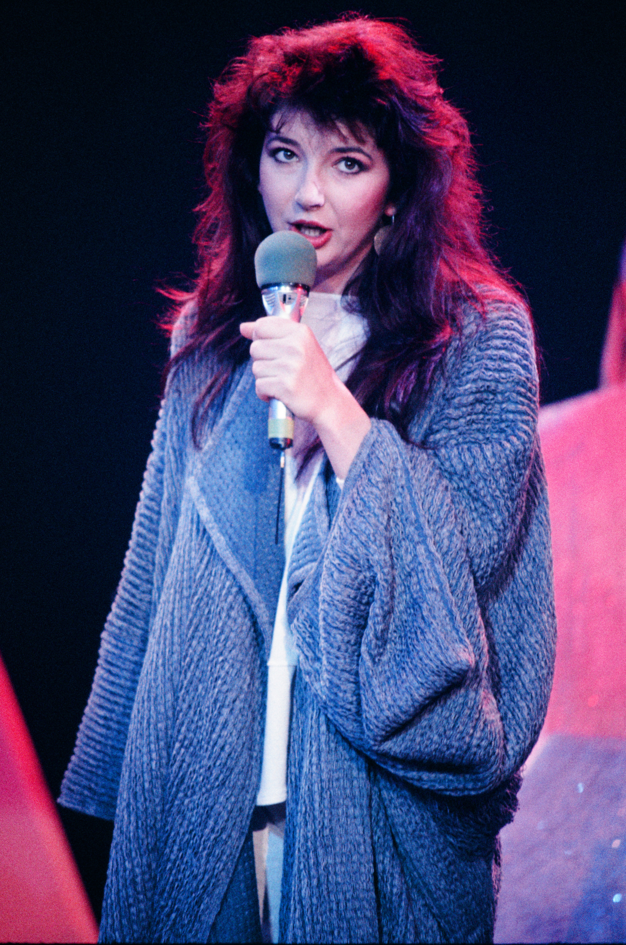 Kate singing into a microphone and wearing a loose coat