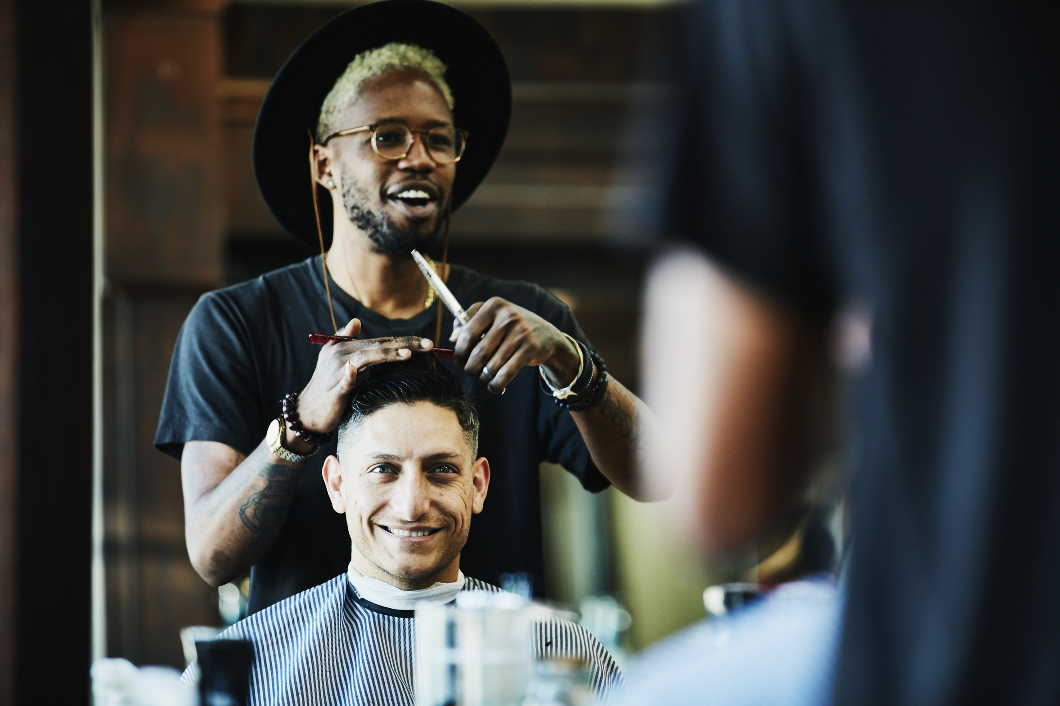 A hairstylist or barber cuts a man&#x27;s hair in front of a mirror