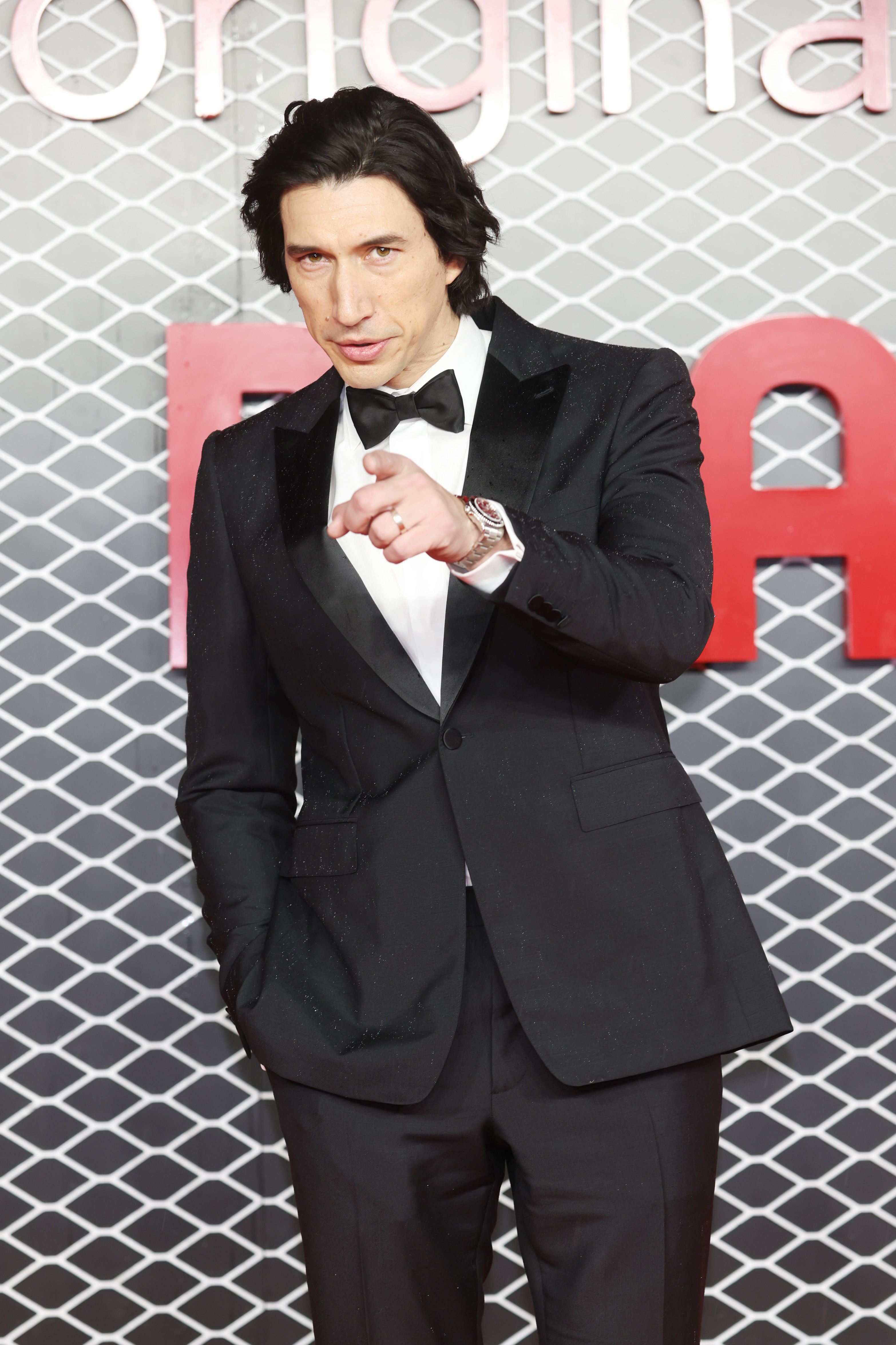 Closeup of Adam Driver in a tux on the red carpet and pointing at the camera