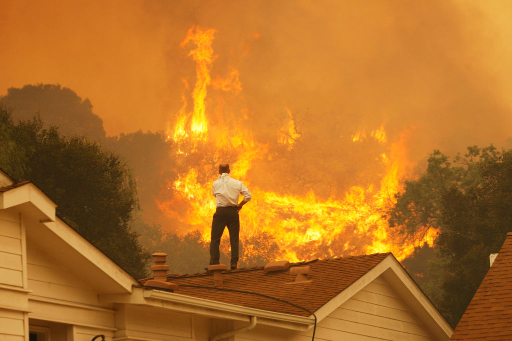 A man on his roof while wildfires rage in the background