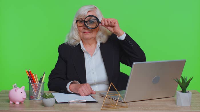 a woman behind her laptop and holding a magnifying glass