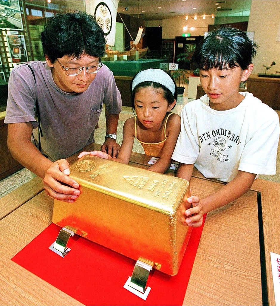 Three people leaning over a huge block of gold on a table
