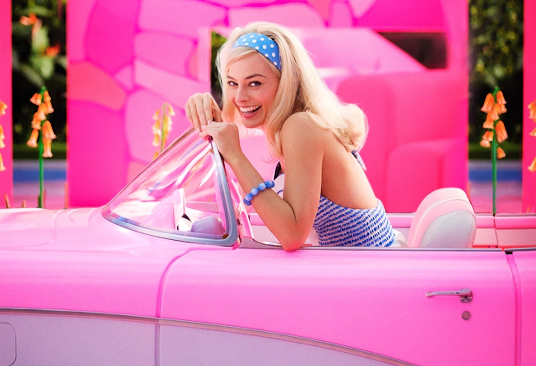 Margot as Barbie smiling while sitting in a Barbie pink convertible