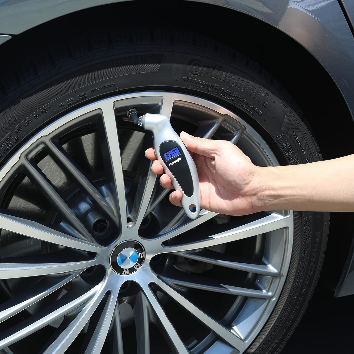 Person inflating car tire with digital tire inflator, vehicle logo visible