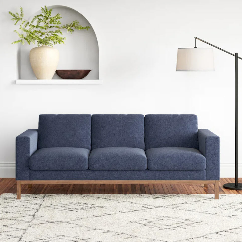 blue three-seater sofa with wooden base next to standing lamp