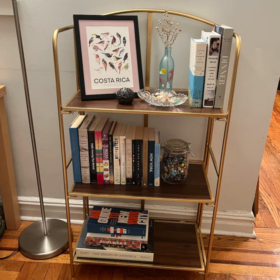gold three-tiered bookshelf with books and framed art