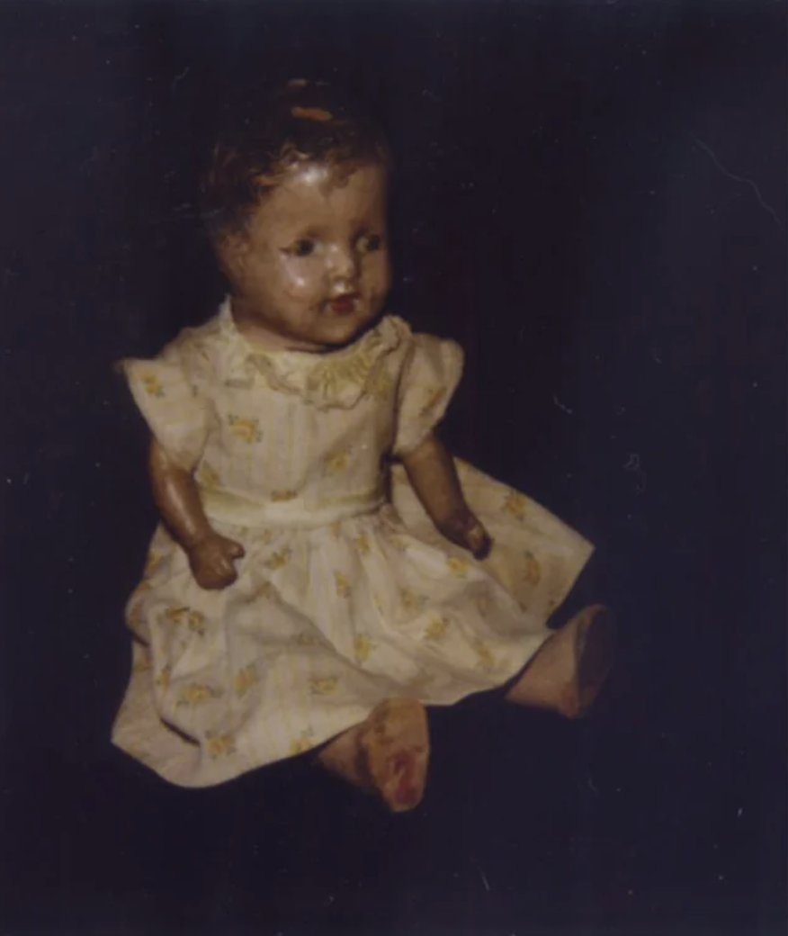 A seated vintage doll with short hair and wearing a print dress