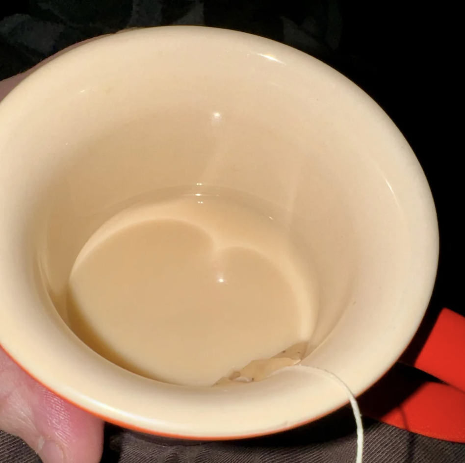 A light beige teacup with a teabag on the side and some chai the exact shade of the cup at the bottom, so that it looks transparent
