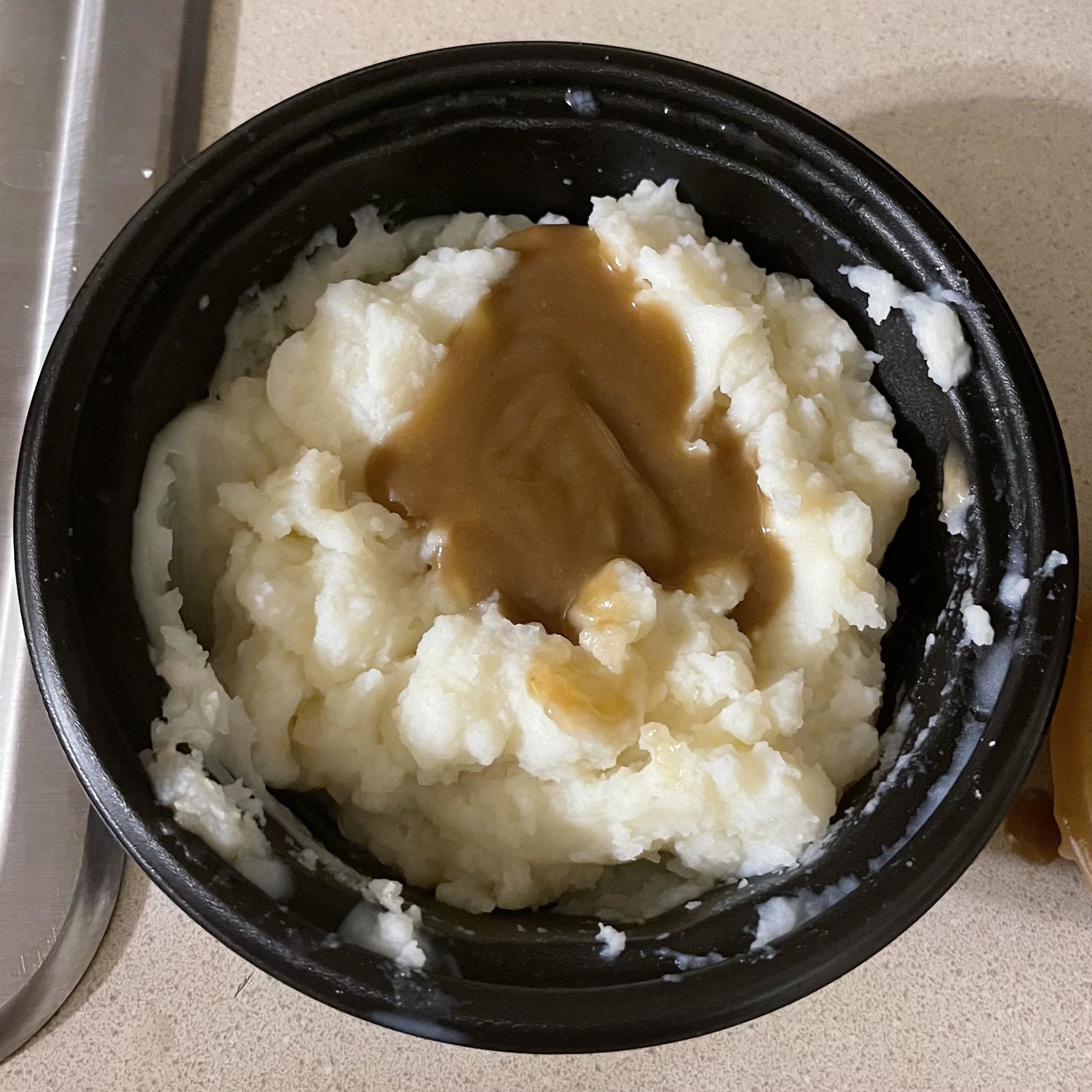 mashed potatoes in a black plastic bowl topped with gravy