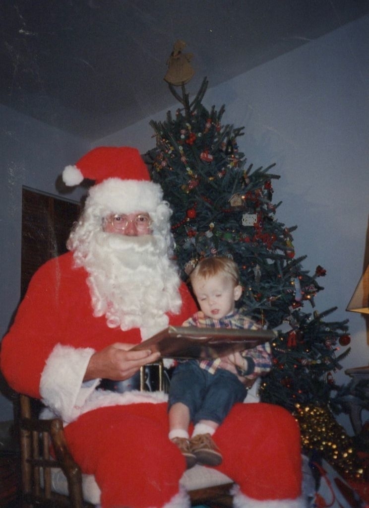 A little boy sitting on Santa's lap in front of a Christmas tree