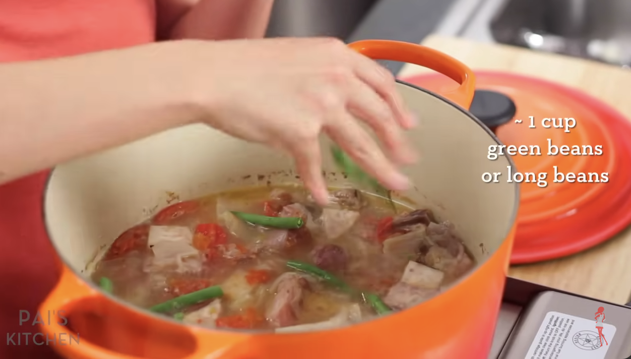 Person adding green beans to a pot of sinigang on the stove