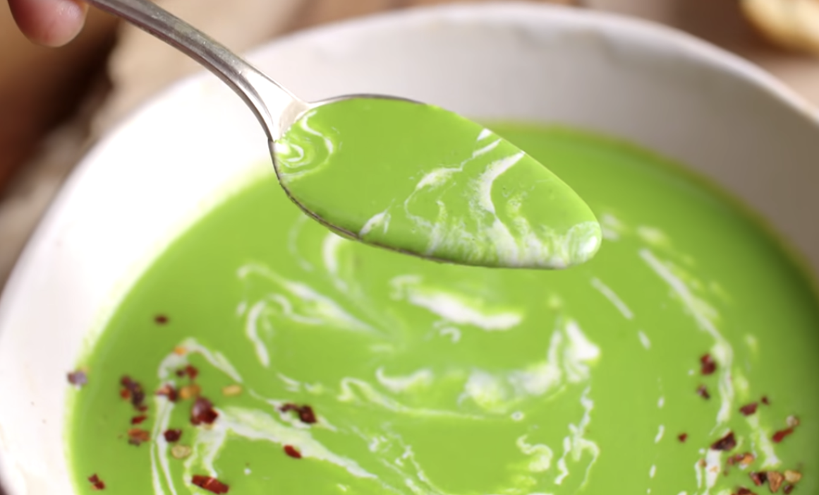 Spoon of cream of spinach soup above a bowl of it