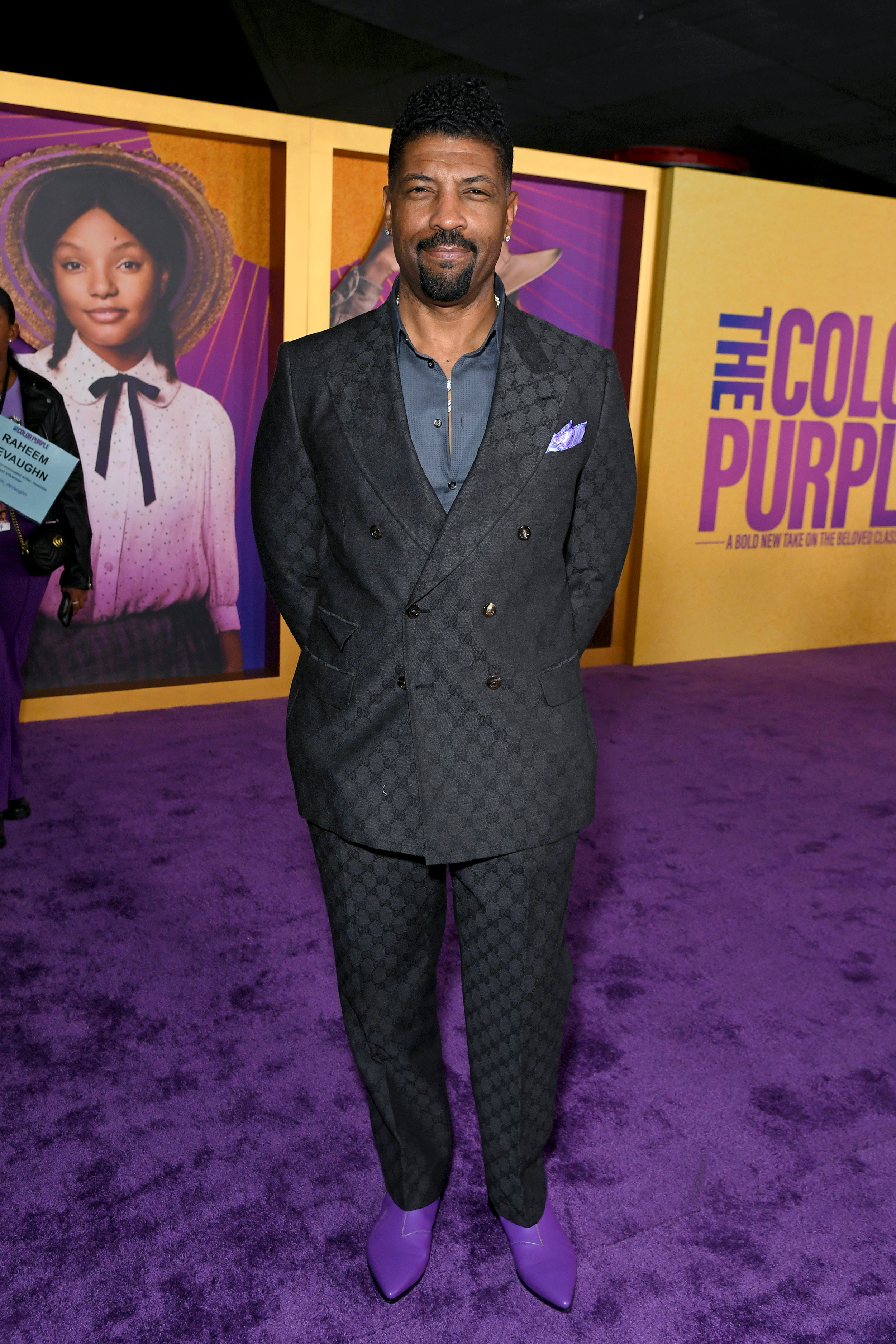 Deon in a black suit, no tie, with purple shoes and a purple handkerchief in the suit jacket pocket