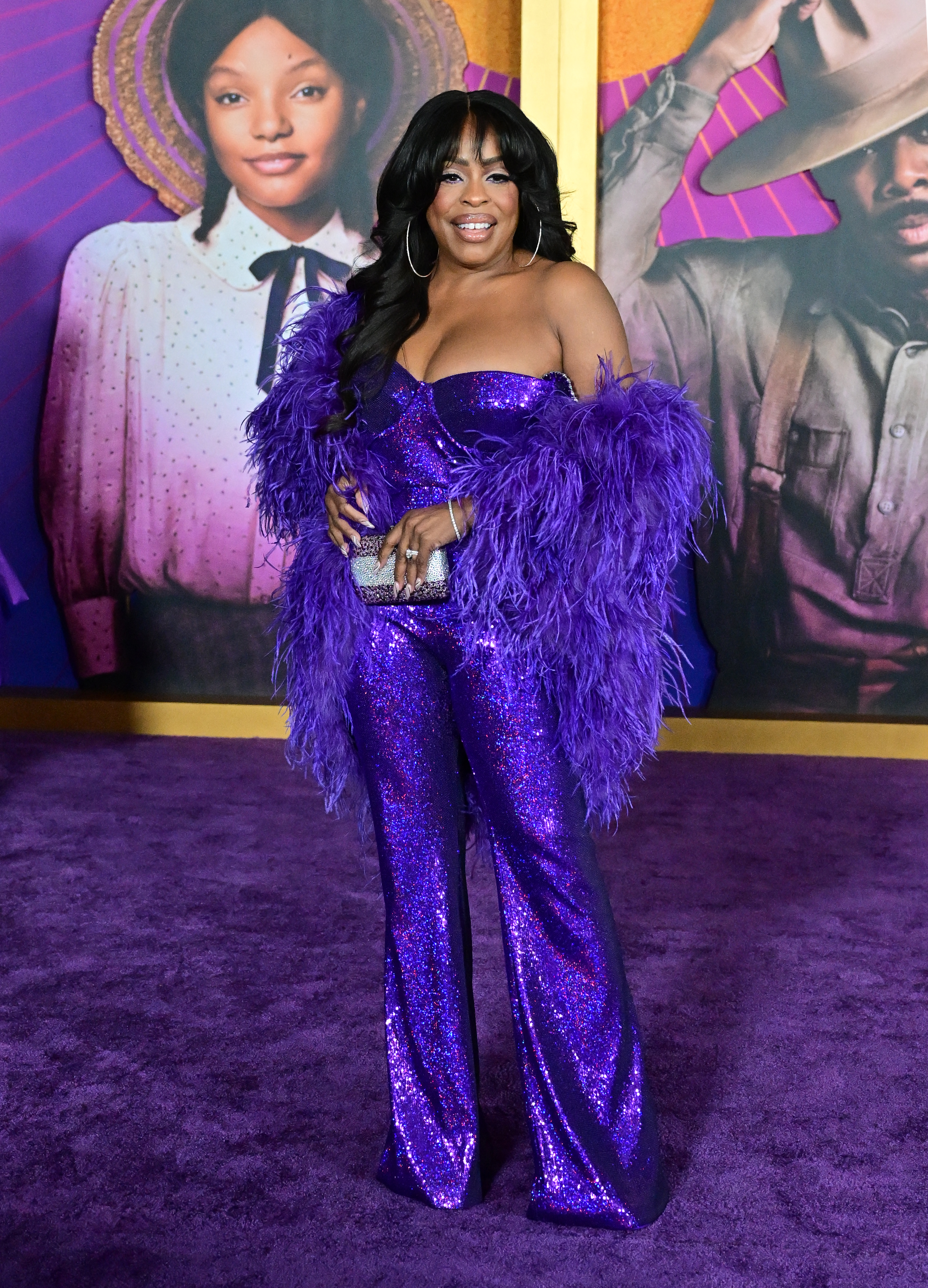 Niecy in a sparkly purple and blue pantsuit with feathery purple cape