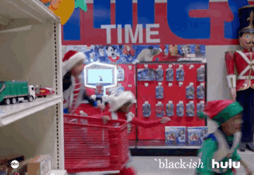 Santa and a bunch of kids race through the store with a cart, filling it with toys.