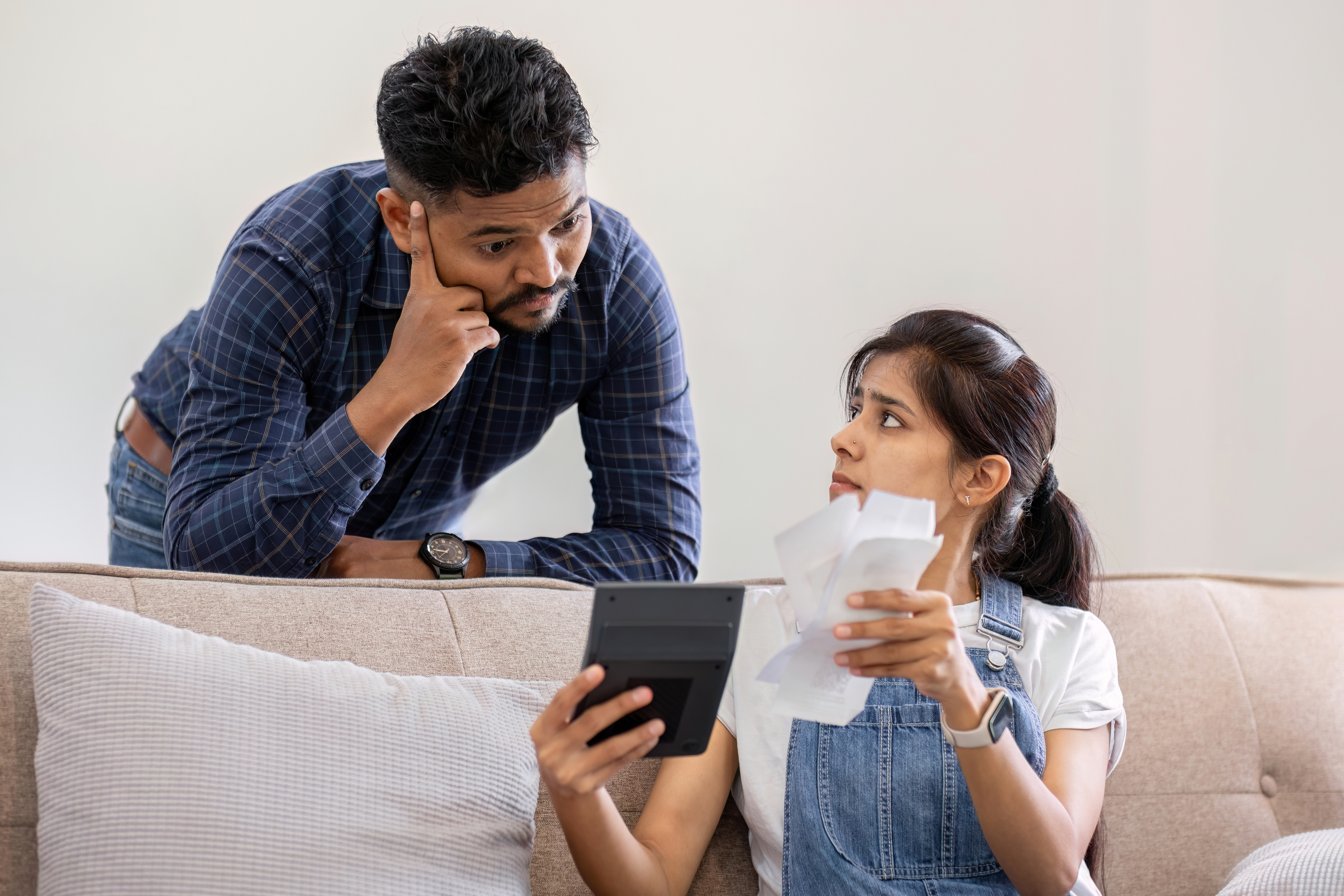A man and a woman at a couch looking at bills and a calculator