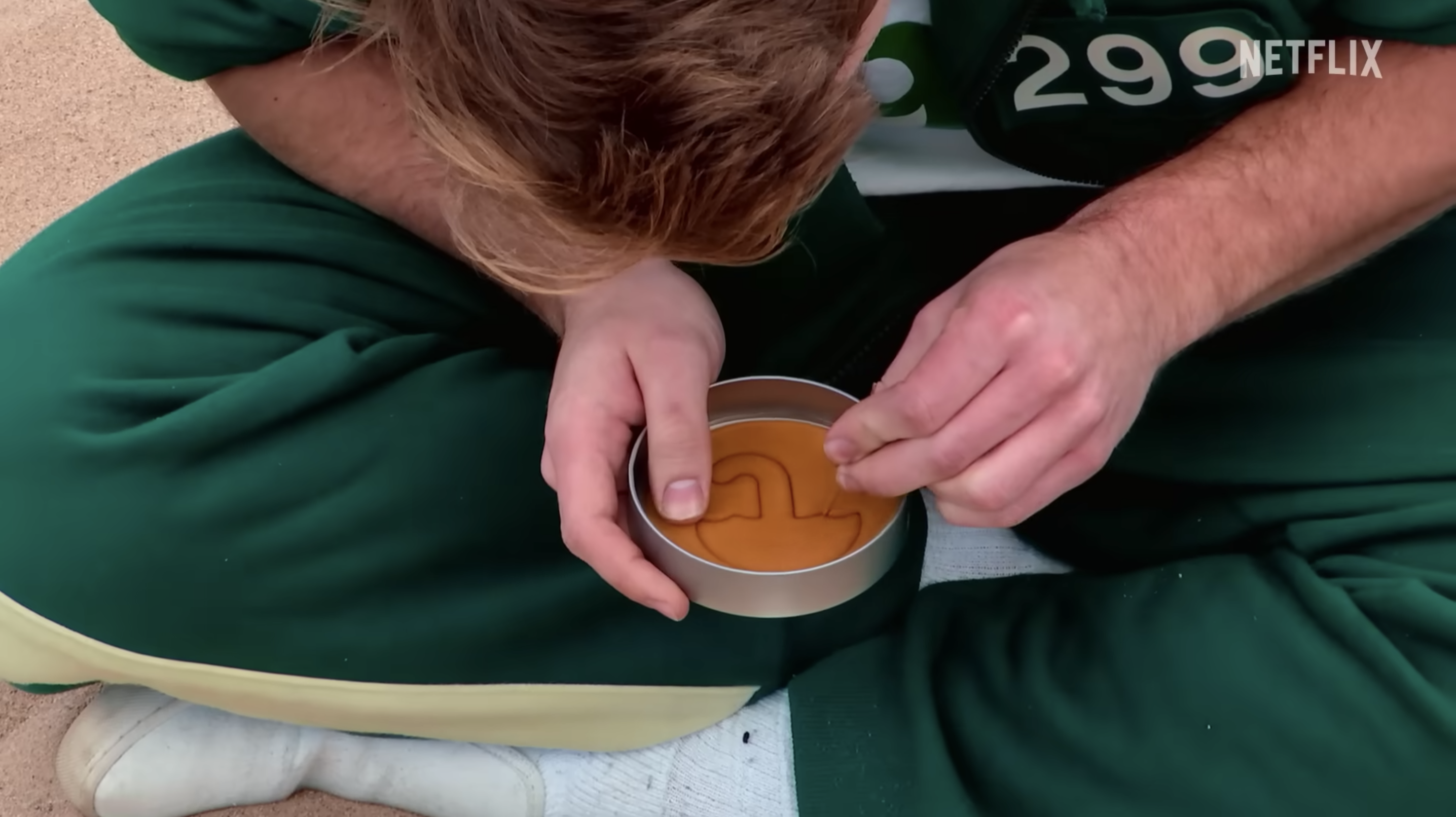 Close-up of player playing Dalgona cookie challenge, cutting out part of a cookie in a tin