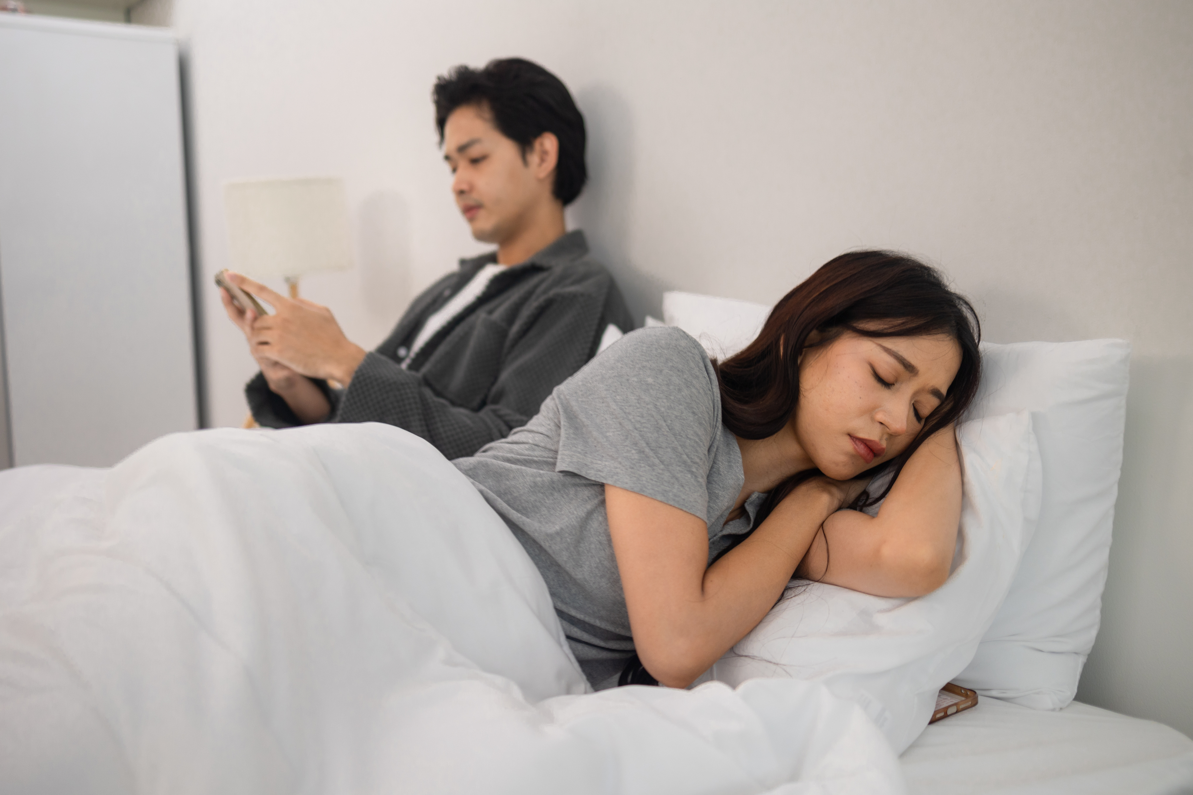 couple in bed. man on phone while woman sleeps