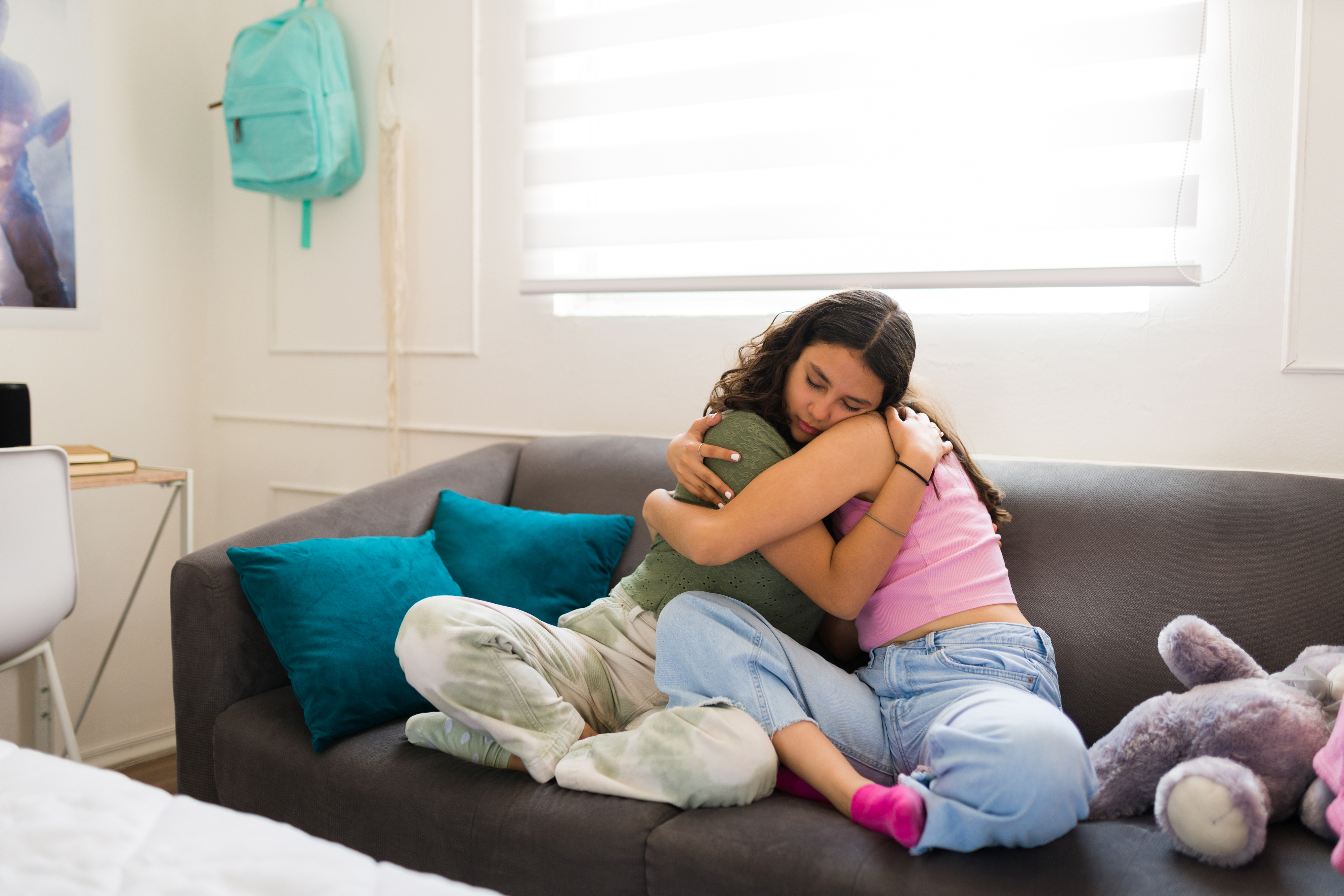 Two dark-haired teen girls hugging on a couch