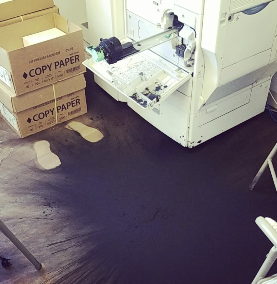 A large ink spill next to a printer that is completely covering the floor