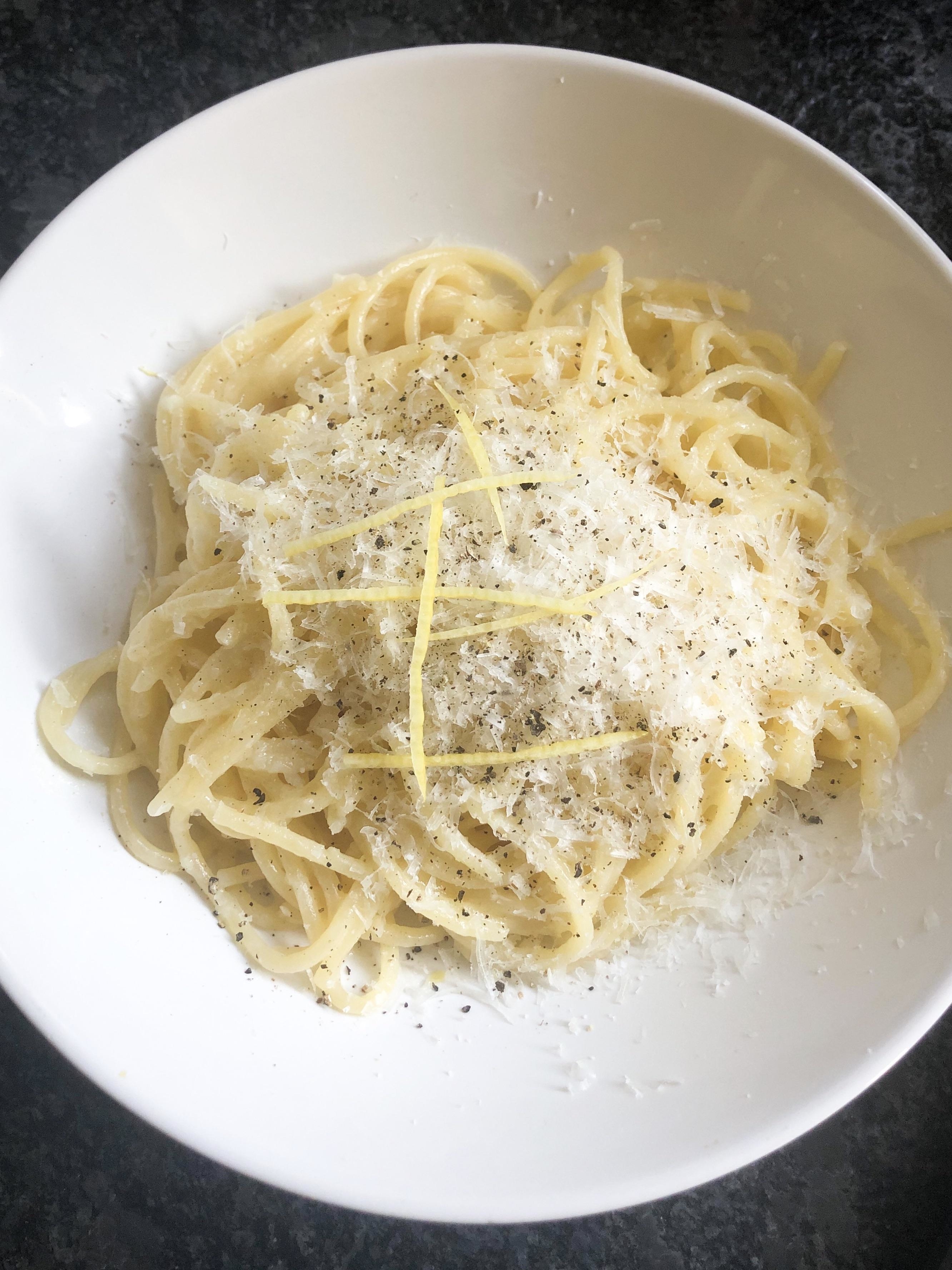 a bowl of spaghetti topped with parmesan and pepper