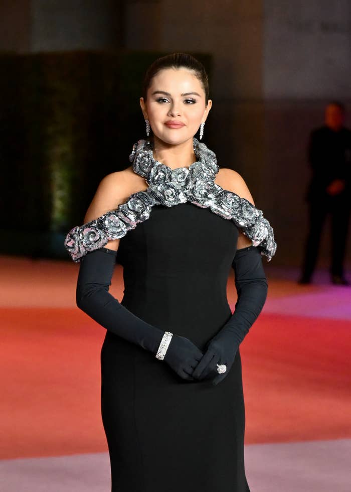 Close-up of Selena smiling at a media event and wearing opera gloves and a gown